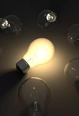 One lit light bulb surrounded by unlit lightbulbs 